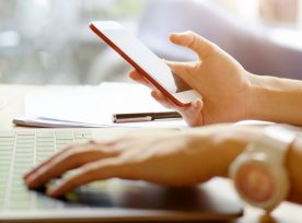 Young Woman Looking Smartphone And Using Laptop Computer While Working In Office.