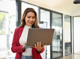 Professional Millennial Asian Businesswoman Stands In Her Office Using Portable Laptop