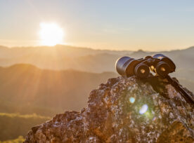 Binoculars On Top Of Rock Mountain At Beautiful Sunset Background.