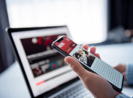 Online News On A Smartphone And Laptop, Woman Reading News Or Articles In A Mobile Phone Screen Application At Home. Newspaper And Portal On Internet.