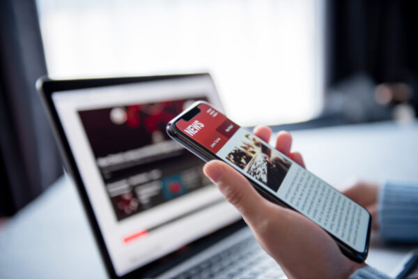 Online News On A Smartphone And Laptop, Woman Reading News Or Articles In A Mobile Phone Screen Application At Home. Newspaper And Portal On Internet.