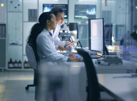 Focused, Serious Medical Scientists Analyzing Research Scans On A Computer, Working Late In The Laboratory. Lab Workers Examine And Talk About Results From A Checkup While Working Overtime