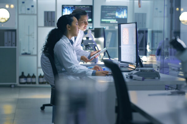 Focused, Serious Medical Scientists Analyzing Research Scans On A Computer, Working Late In The Laboratory. Lab Workers Examine And Talk About Results From A Checkup While Working Overtime