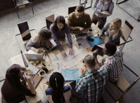 Top View Of Mixed Race Business Team Sitting At The Table At Loft Office And Working. Woman Manager Brings The Document