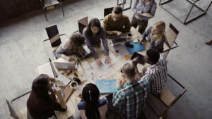 Top View Of Mixed Race Business Team Sitting At The Table At Loft Office And Working. Woman Manager Brings The Document