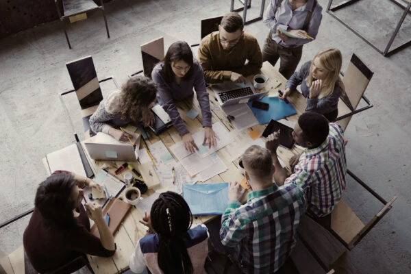 Top View Of Mixed Race Business Team Sitting At The Table At Loft Office And Working. Woman Manager Brings The Document