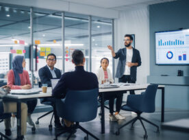 Diverse Modern Office: Businessman Leads Business Meeting With Managers, Talks, Uses Presentation Tv With Statistics, Infographics. Digital Entrepreneurs Work On E Commerce Project.