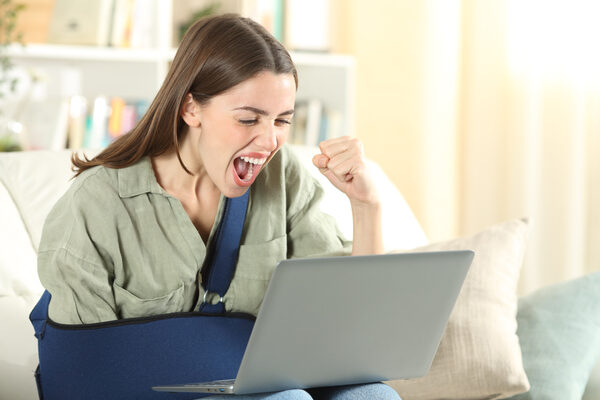 Excited Disabled Woman With Broken Arm Using Accessible Website On Laptop