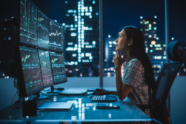 Portrait Of A Financial Analyst Working On Computer With Multi Monitor Workstation With Real Time Stocks, Commodities And Exchange Market Charts. Businesswoman At Work In Investment Broker Agency.