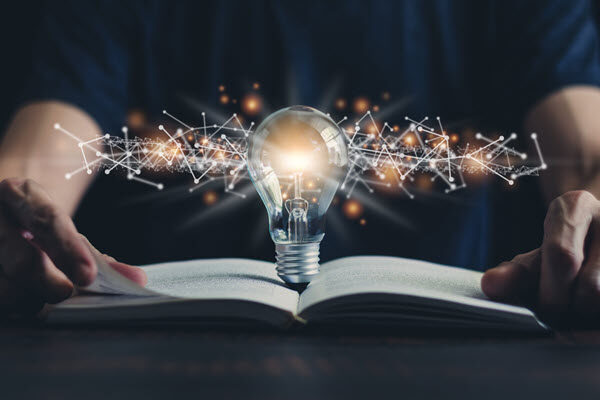 Image of an open book with a light bulb and connected dots that look like digital neurons. This signifies that intentional corporate innovation can evolve if managed well.