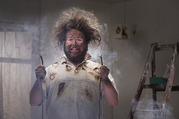 Funny picture of a man holding frayed electrical wires, his hair is standing on end with face scorched.