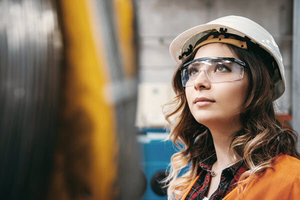 A woman in hardhat and safety glasses working in manufacturing.