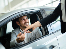 Man sits in car and receives keys to the car after a sale.