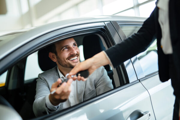 Man sits in car and receives keys to the car after a sale.