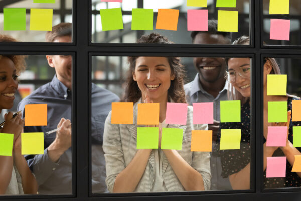 Happy Mixed Race Group Looking At Notes On Glass Board.