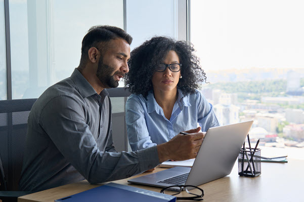 tiethnic colleagues sitting at desk looking at laptop computer in office. stock photo