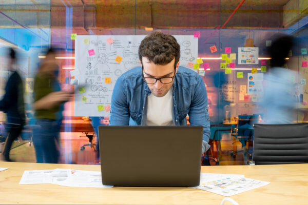 Man Working At A Creative Office Using His Computer And People Moving At The Background