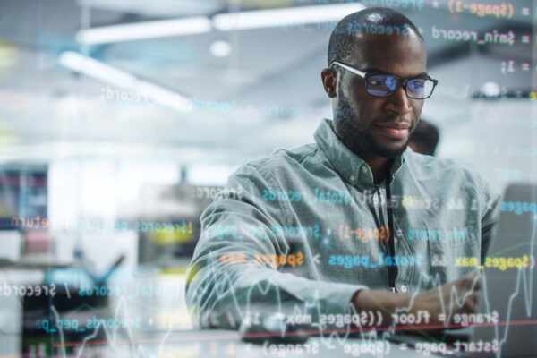 Modern Office: Portrait Of Motivated Black It Programmer Working On Laptop Computer. Male Specialist Create Website, Software Engineer Develop Programme. Shot With Visual Effects Of Running Code.