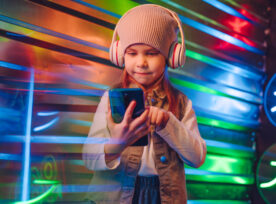 Little Girl Wearing Headphones Using Smartphone on the Colorful Neon