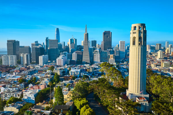 Aerial Coit Tower In Late Afternoon With Downtown San Francisco Skyscrapers And Distant Bridge