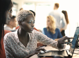 Woman pointing at computer screen showing coworker the work she's doing.