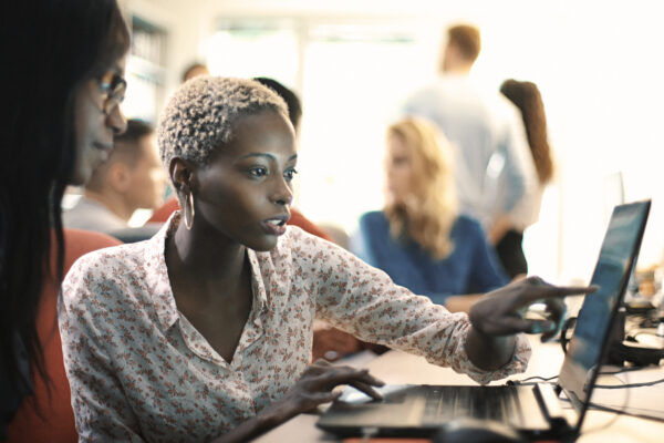 Woman pointing at computer screen showing coworker the work she's doing.