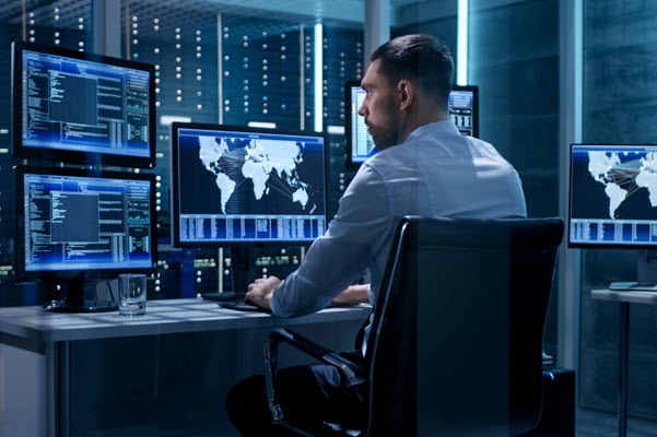 Technical Controller Working at His Workstation with Multiple Displays. Displays Show Various Technical Information. He's Alone in System Control Center.