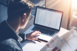 Closeup View Of Banking Finance Analyst In Eyeglasses Working At Sunny Office On Laptop While Sitting At Wooden Table.businessman Analyze Stock Report On Notebook Screen.blurred Background,horizontal.