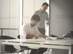 Two Business Men Working Together In Office. Reading Document.