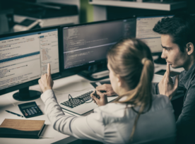 Woman and man looking at two computer screens, woman pointing at screen.