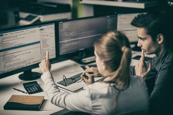 Woman and man looking at two computer screens, woman pointing at screen.