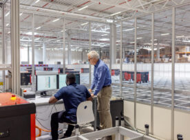 Manager With A Male Worker Working On Computer In Agv Control Room At Warehouse