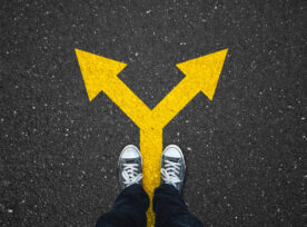 Photo looking down at legs standing on asphalt with yellow directional arrows pointing in different directions.