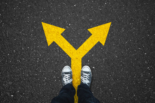 Photo looking down at legs standing on asphalt with yellow directional arrows pointing in different directions.