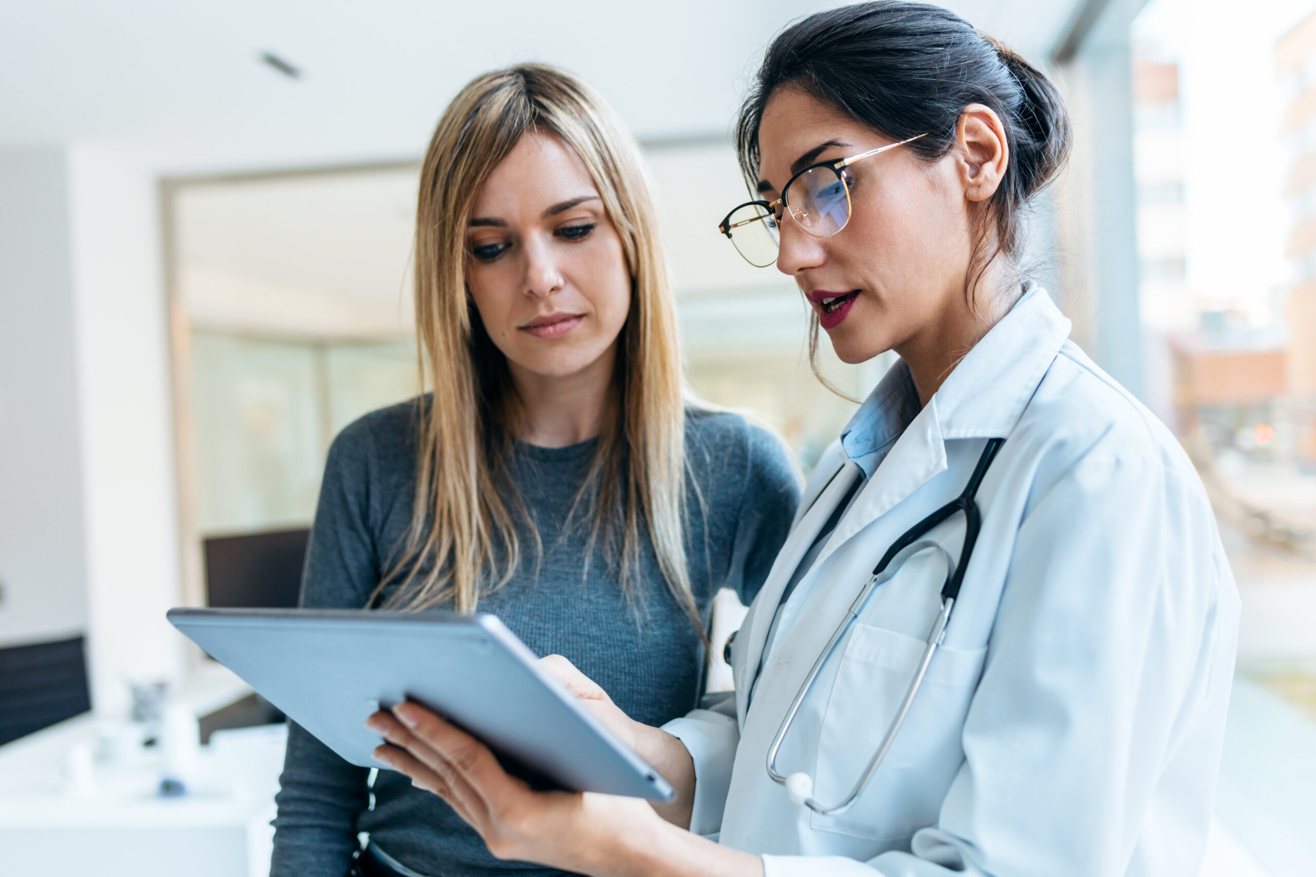 Female Doctor Talking While Explaining Medical Treatment With Digital Tablet To Patient In The Consultation.